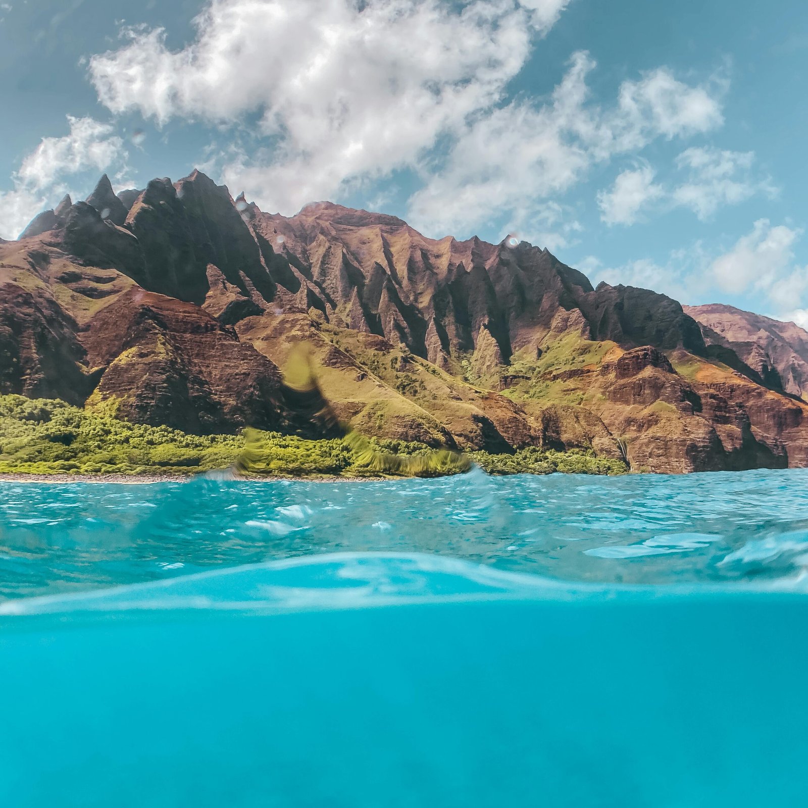 Captivating view of the Na Pali coastline with clear turquoise waters, showcasing dramatic cliffs under a sunny sky.